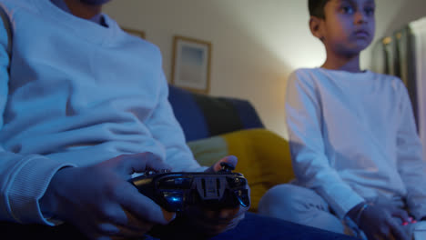 Primer-Plano-De-Las-Manos-De-Dos-Niños-Pequeños-En-Casa-Jugando-Con-Una-Consola-De-Juegos-De-Computadora-En-La-Televisión-Sosteniendo-Controladores-A-Altas-Horas-De-La-Noche-5